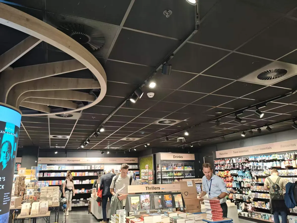 Black surface-mounted track and anti-glare LED track spotlights installed on a dark exposed grid ceiling above bookstore shelving