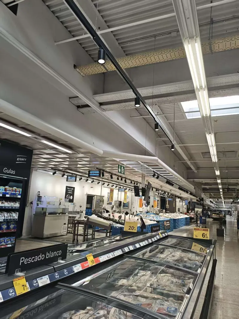 Aimed track spotlights lighting a supermarket fresh food counter under an exposed ceiling