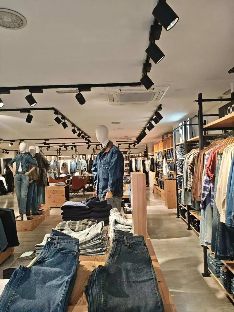 Black track and cylindrical spotlights on a white ceiling above apparel and denim displays